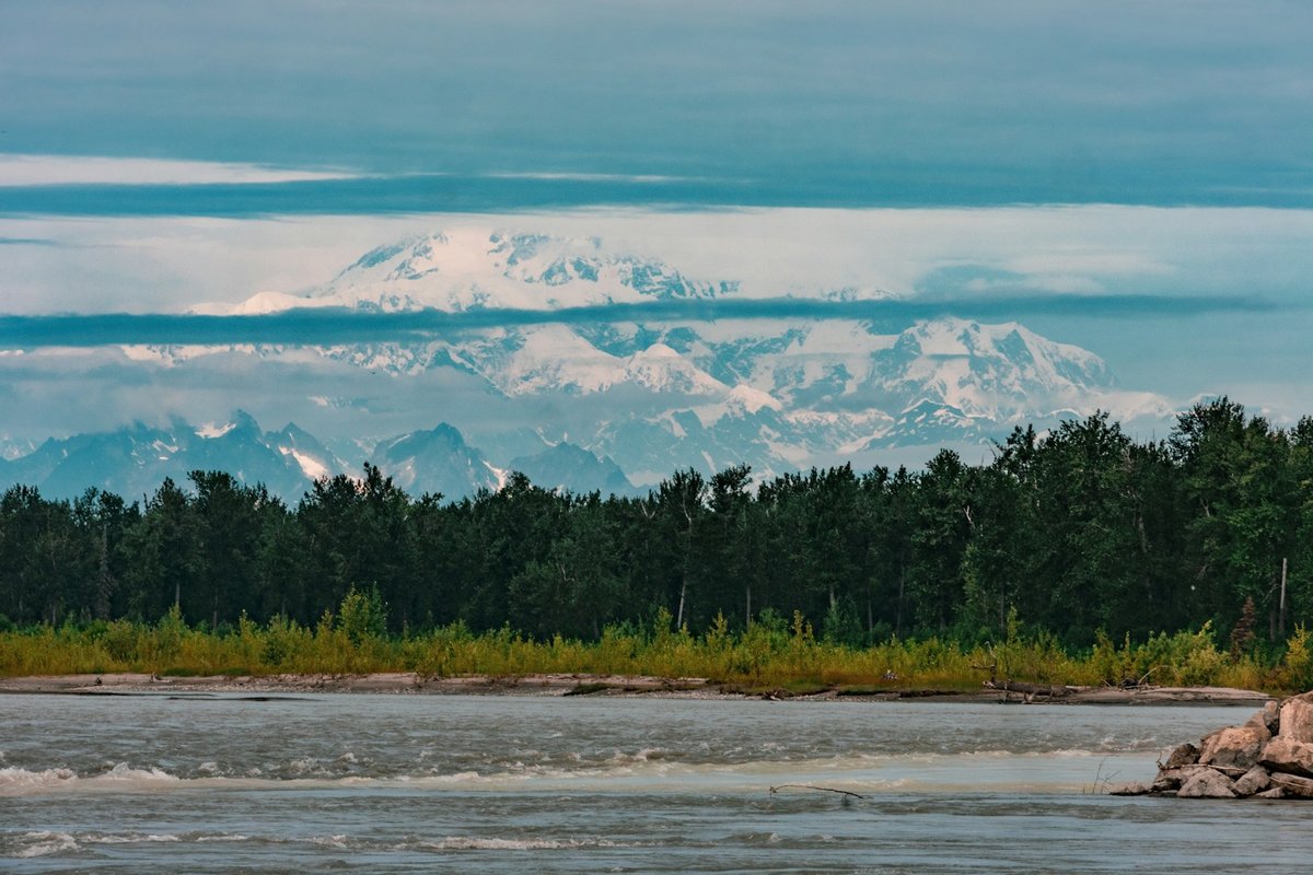 A mountain range rising above a river and trees near Talkeetna, Alaska