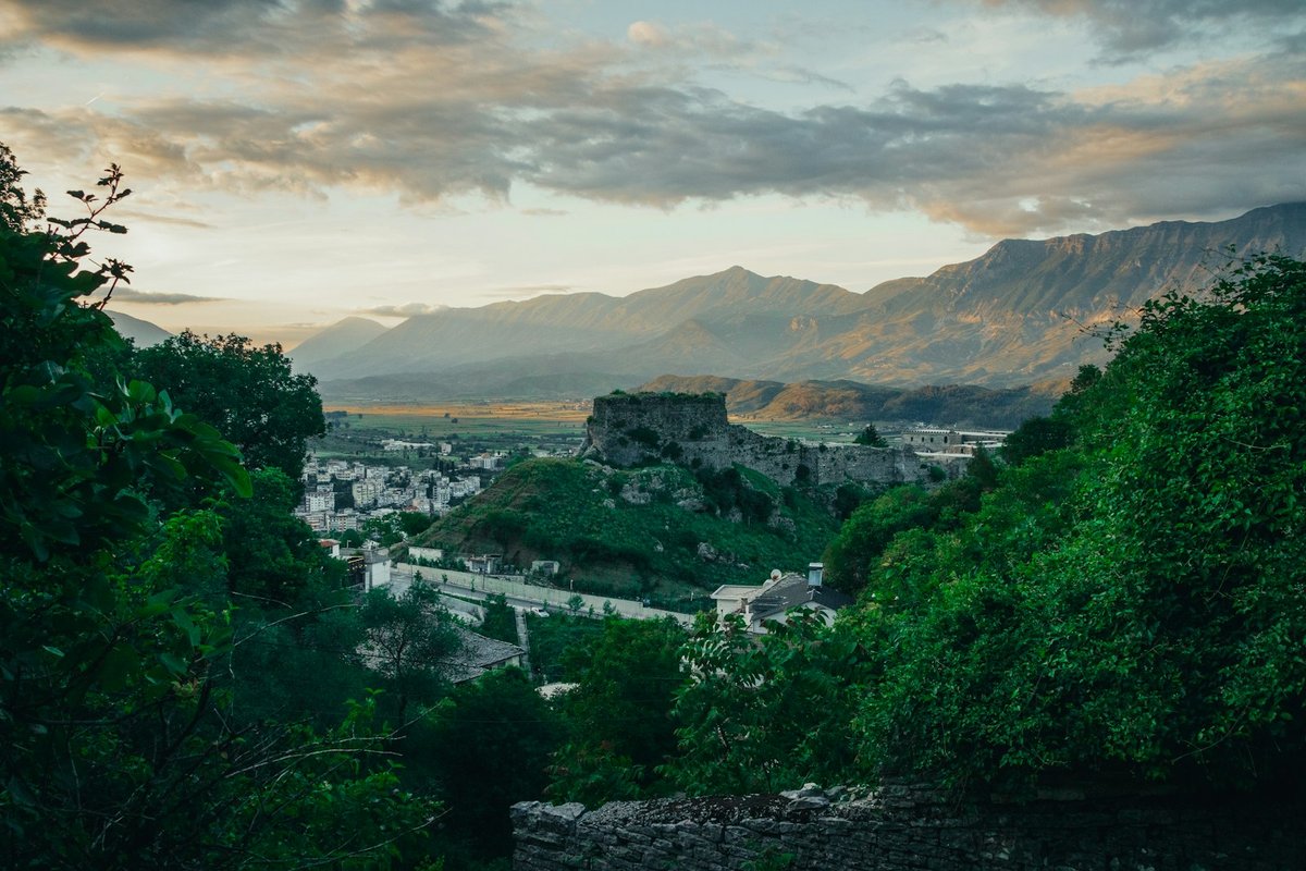 Gjirokastër Castle on a hill above green slopes, with mountains behind