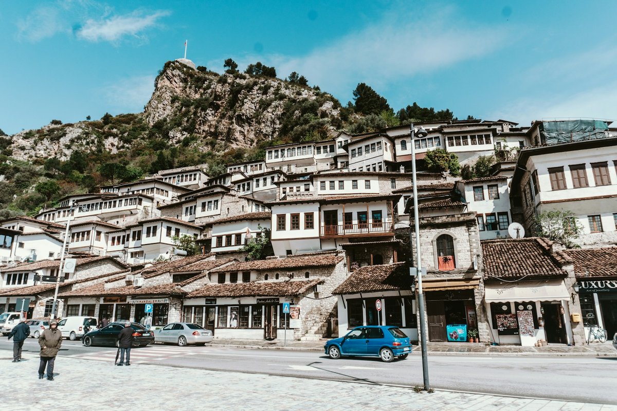 White Ottoman-era houses stacked along a hillside in Berat, Albania, beneath a rocky castle ridge