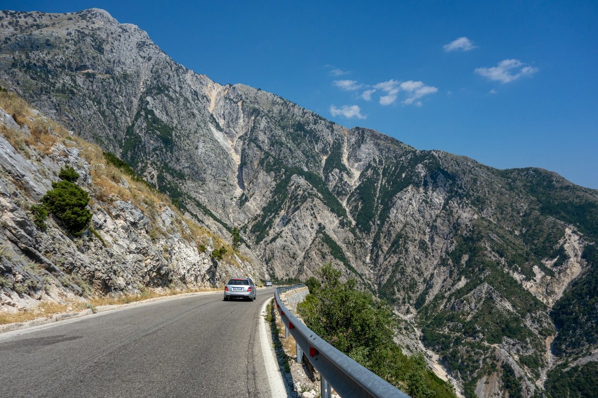 A car on a winding mountain road through the Llogara Pass in Albania, with blue peaks beyond