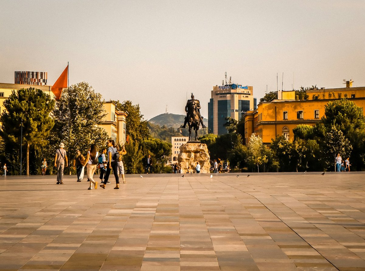 People walking across Skanderbeg Square in Tiranë, with the Skanderbeg statue in the open pedestrian space