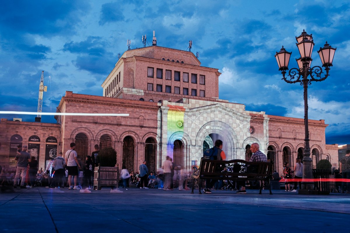 The pink-tuff History Museum of Armenia on Republic Square at dusk, with people sitting on benches in the foreground