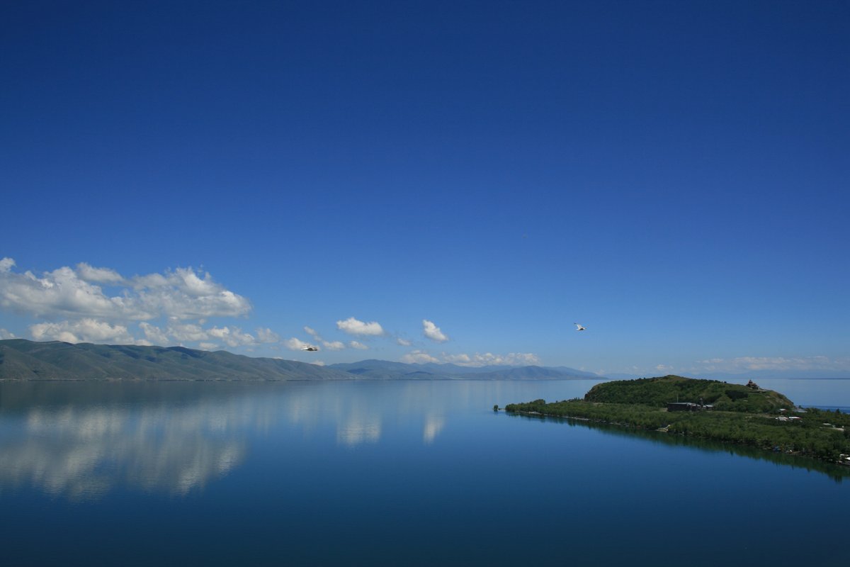 Calm blue water of Lake Sevan with the forested Sevanavank peninsula stretching into the lake