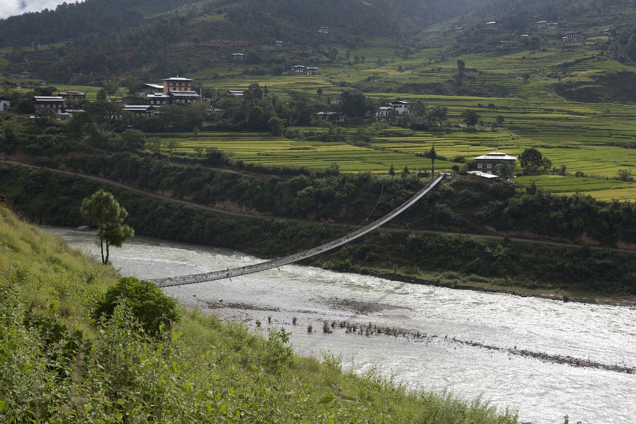 Long suspension bridge decorated with prayer flags over a river in Punakha