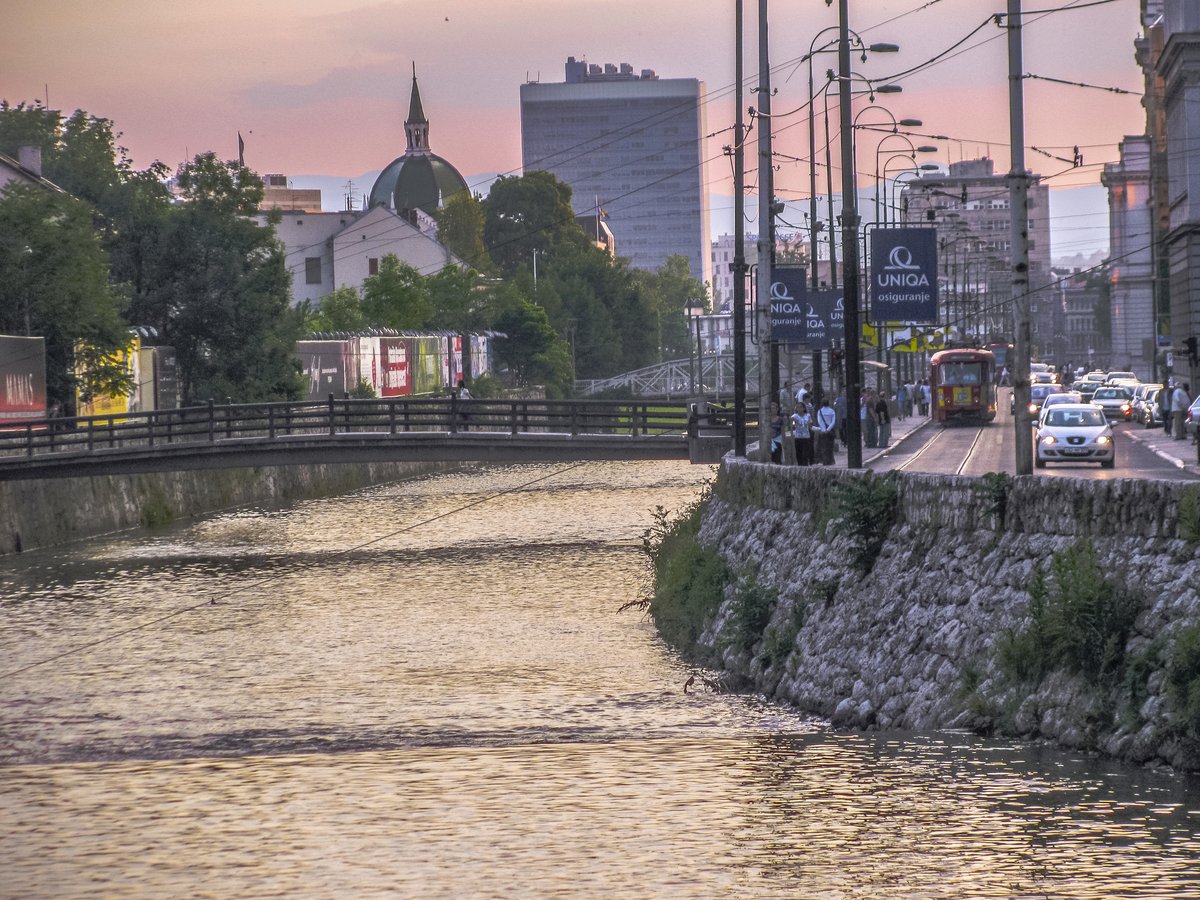 The Miljacka River running through historic Sarajevo at sunset, with bridges and city buildings along the banks