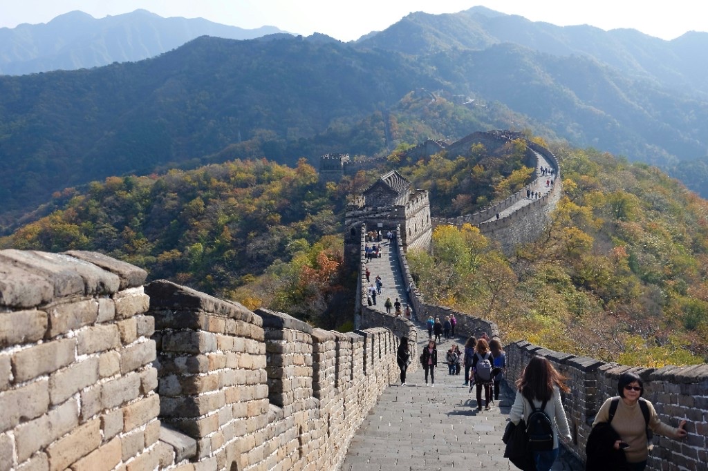 Great Wall of China snaking over forested mountain ridges with a watchtower and visitors on the path