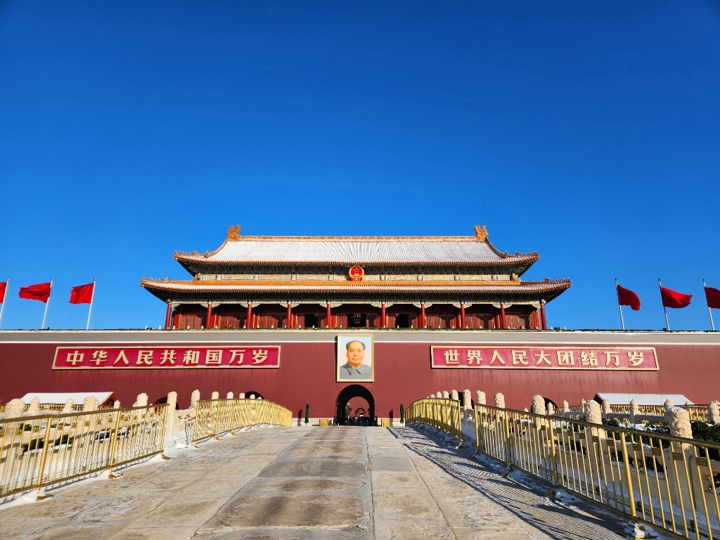 Tiananmen Gate in Beijing with red flags and a clear blue sky, viewed along the stone walkway