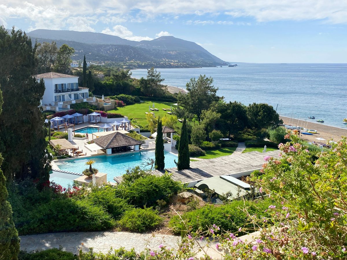 A scenic coastal view of Paphos, Cyprus, with gardens and a pool above the Mediterranean shoreline and mountains in the distance