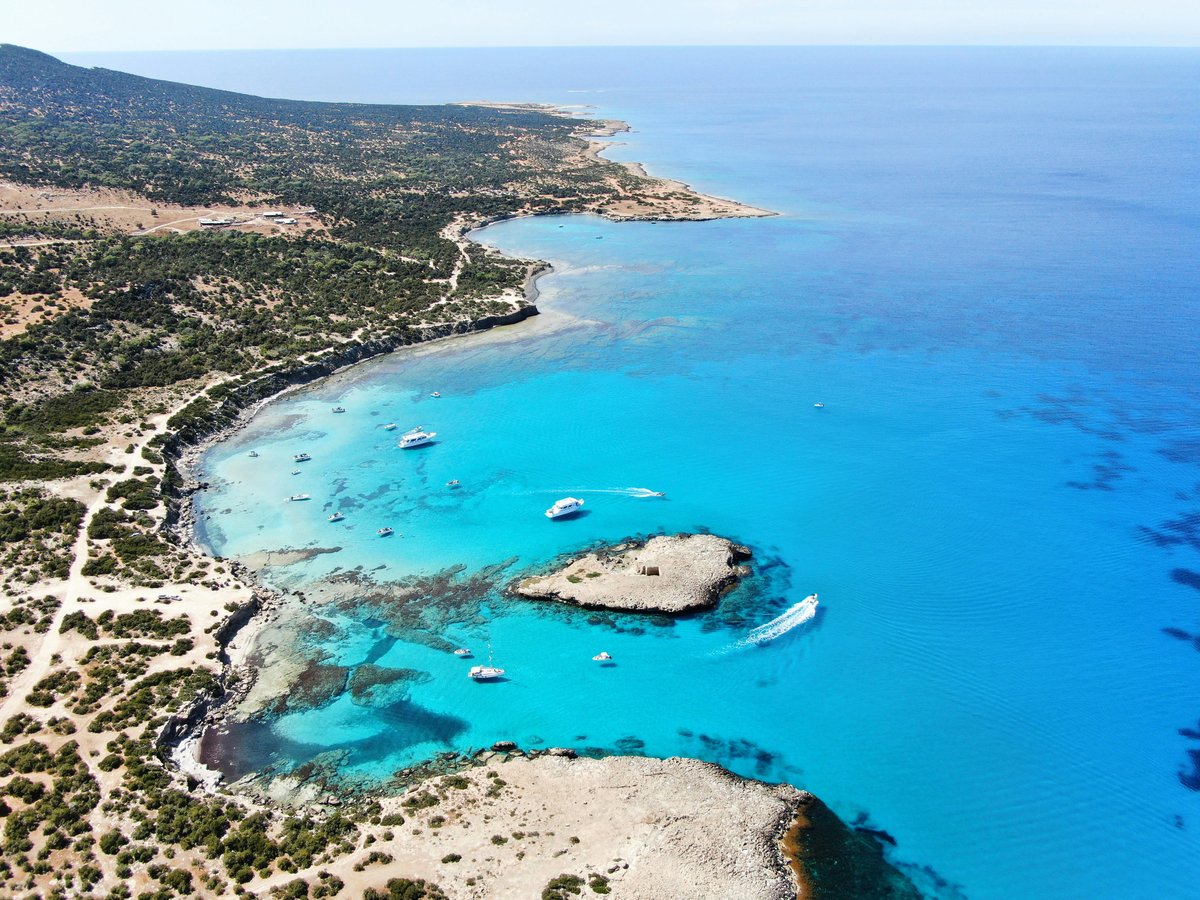 Aerial view of a turquoise bay with boats, rocky headlands and a small island on the Paphos coast of Cyprus