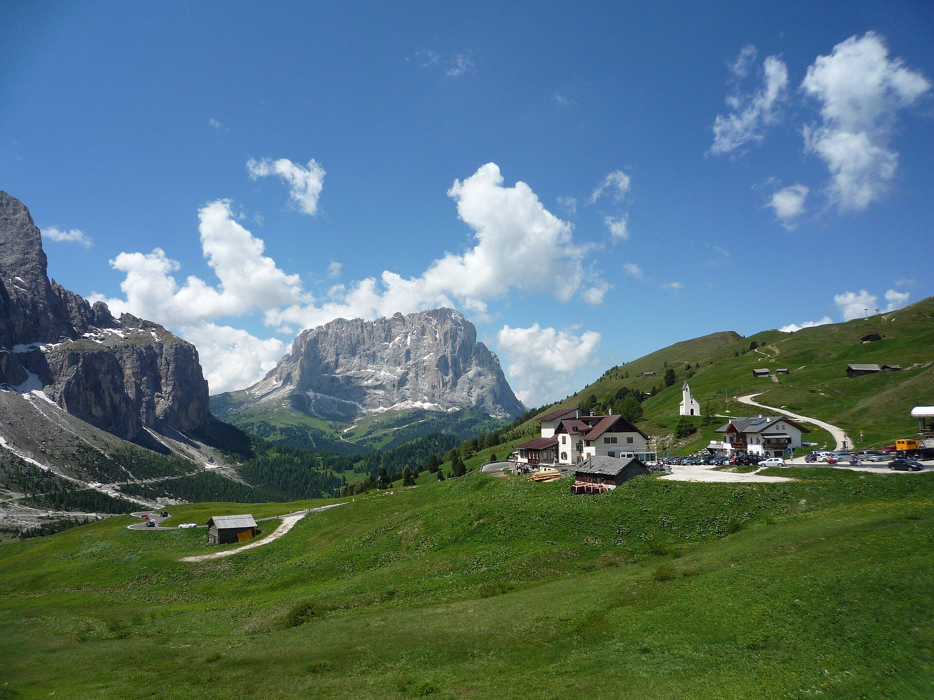Passo Gardena in the Dolomites, with green alpine meadows, mountain huts, winding roads and dramatic peaks surrounding the pass