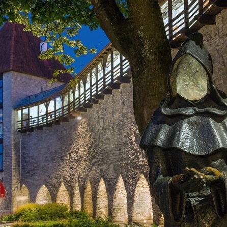 Murallas de la Ciudad Vieja de Tallin al atardecer, estatua de monje y pasarela de madera