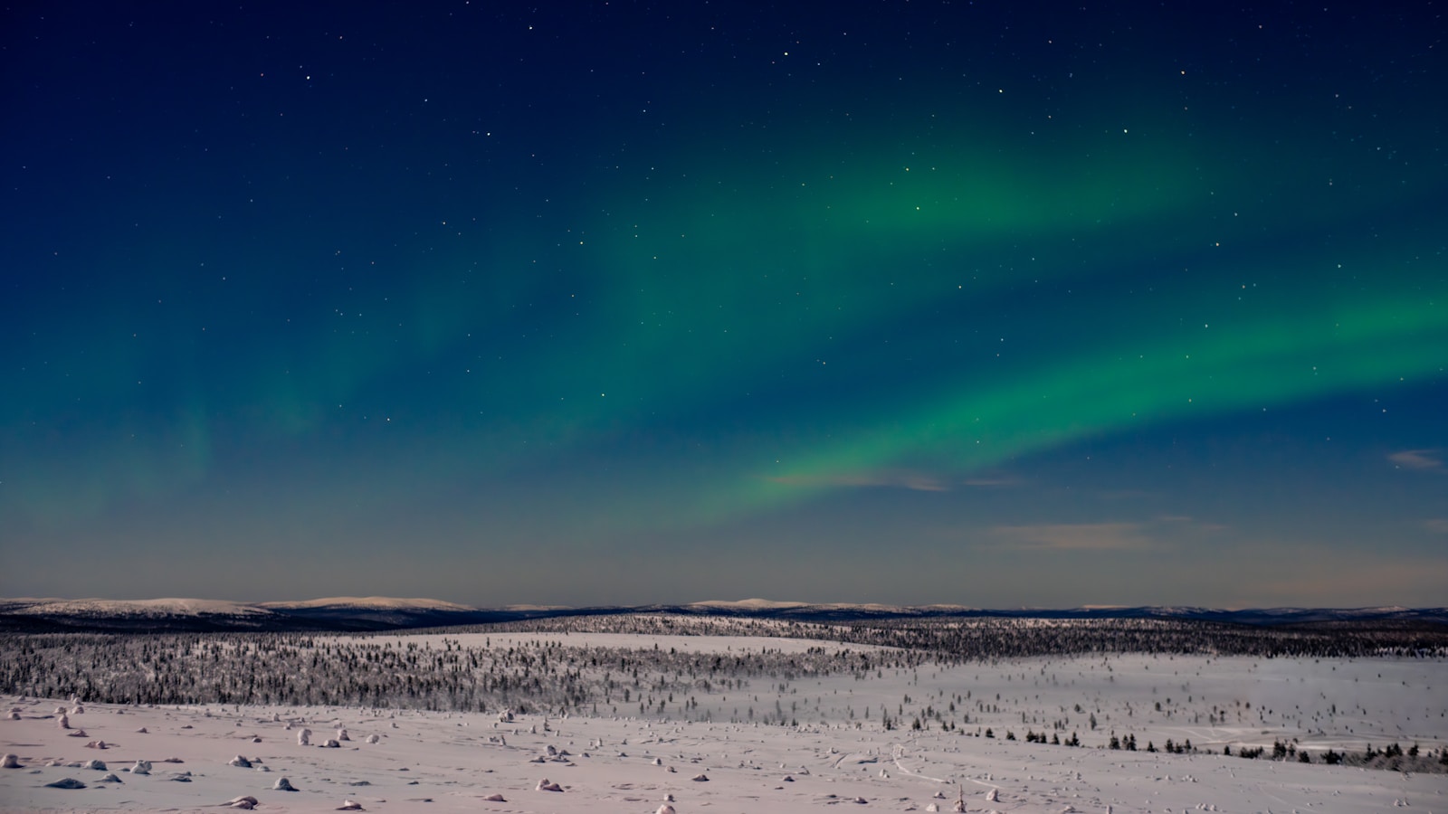 Green aurora waves illuminating a vast snowy Finnish Lapland landscape at night