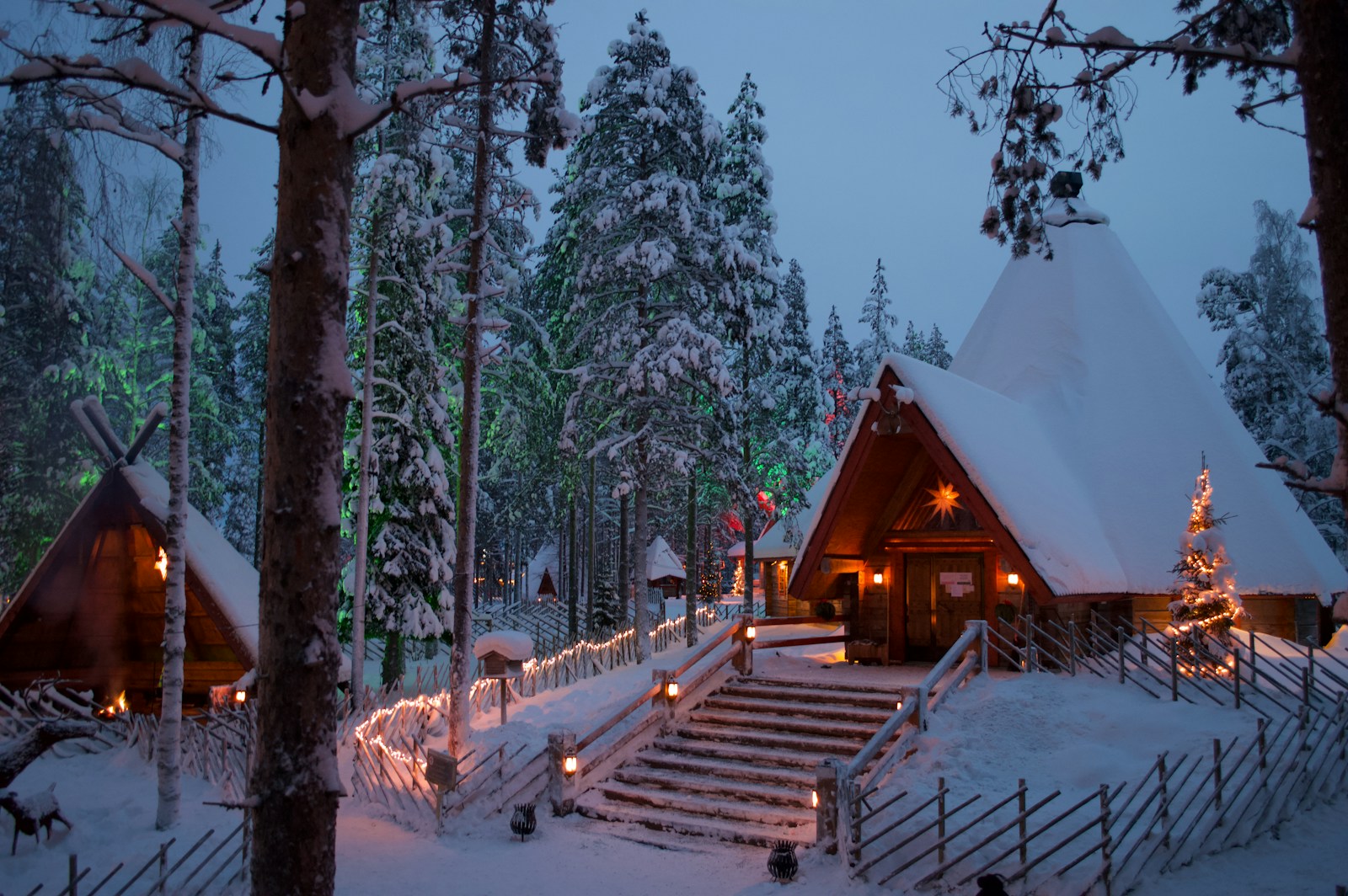 Snow-covered wooden cabin and kota firelight in a Finnish Lapland forest at blue hour