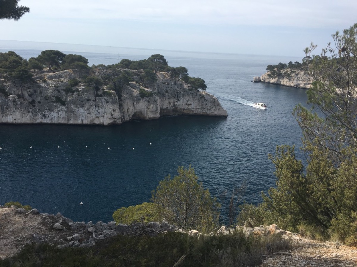 A Calanques cove with white limestone cliffs and a small boat entering deep blue water