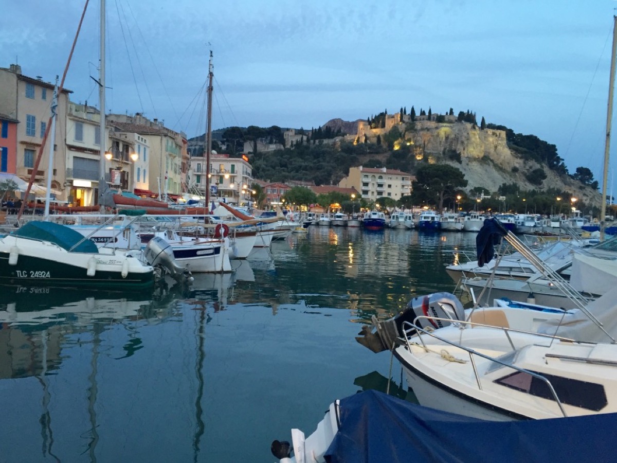 Fishing boats in Cassis harbor with pastel waterfront buildings and the cliffs of Cap Canaille in the background