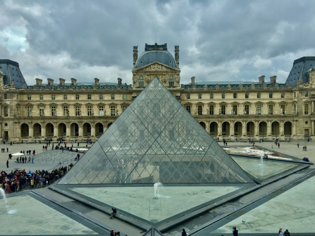 The Louvre Pyramid in Paris framed by the historic palace courtyard under dramatic clouds