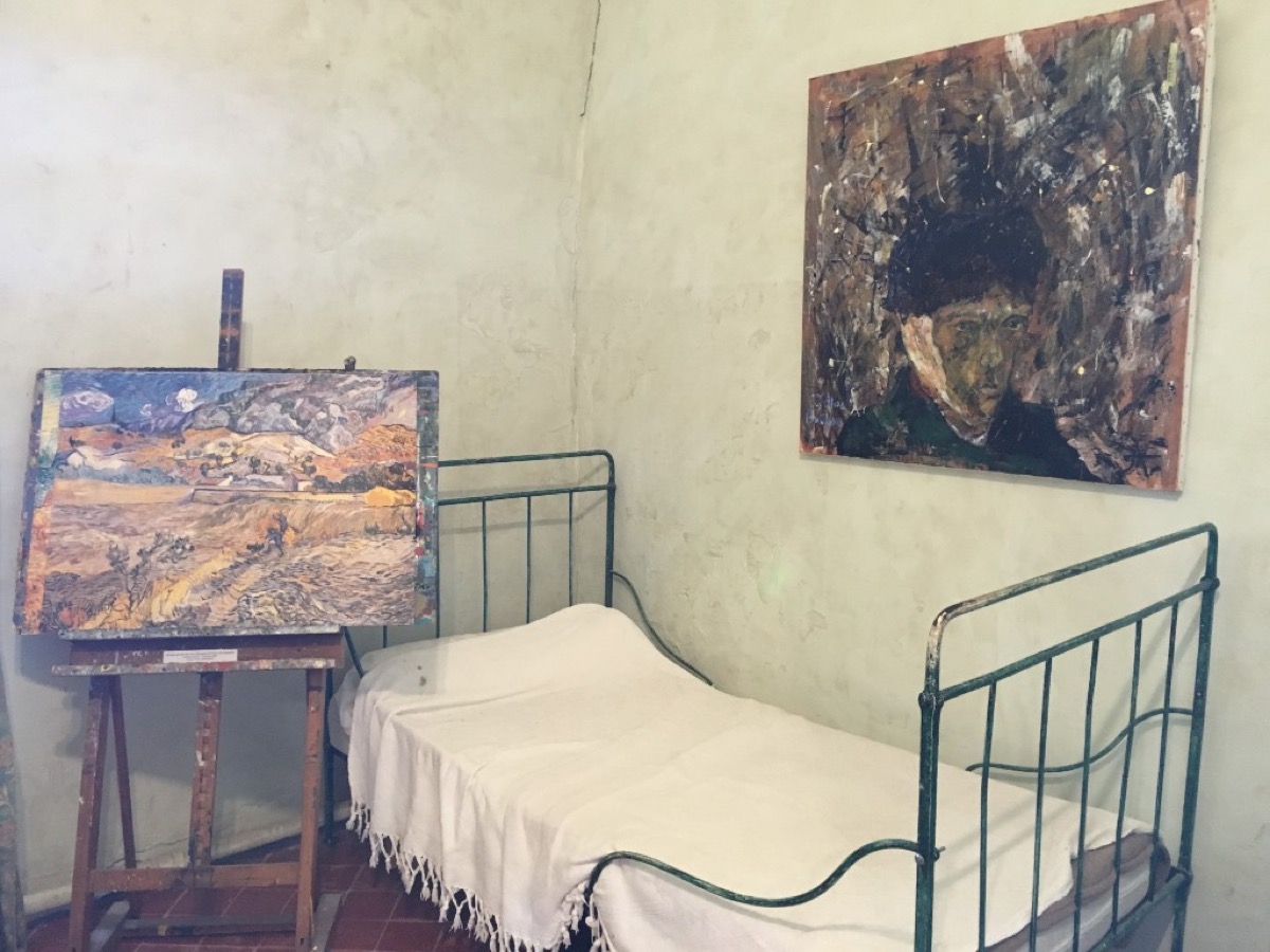 A modest room display at Saint-Paul de Mausole with Van Gogh-themed artwork and a simple iron bed