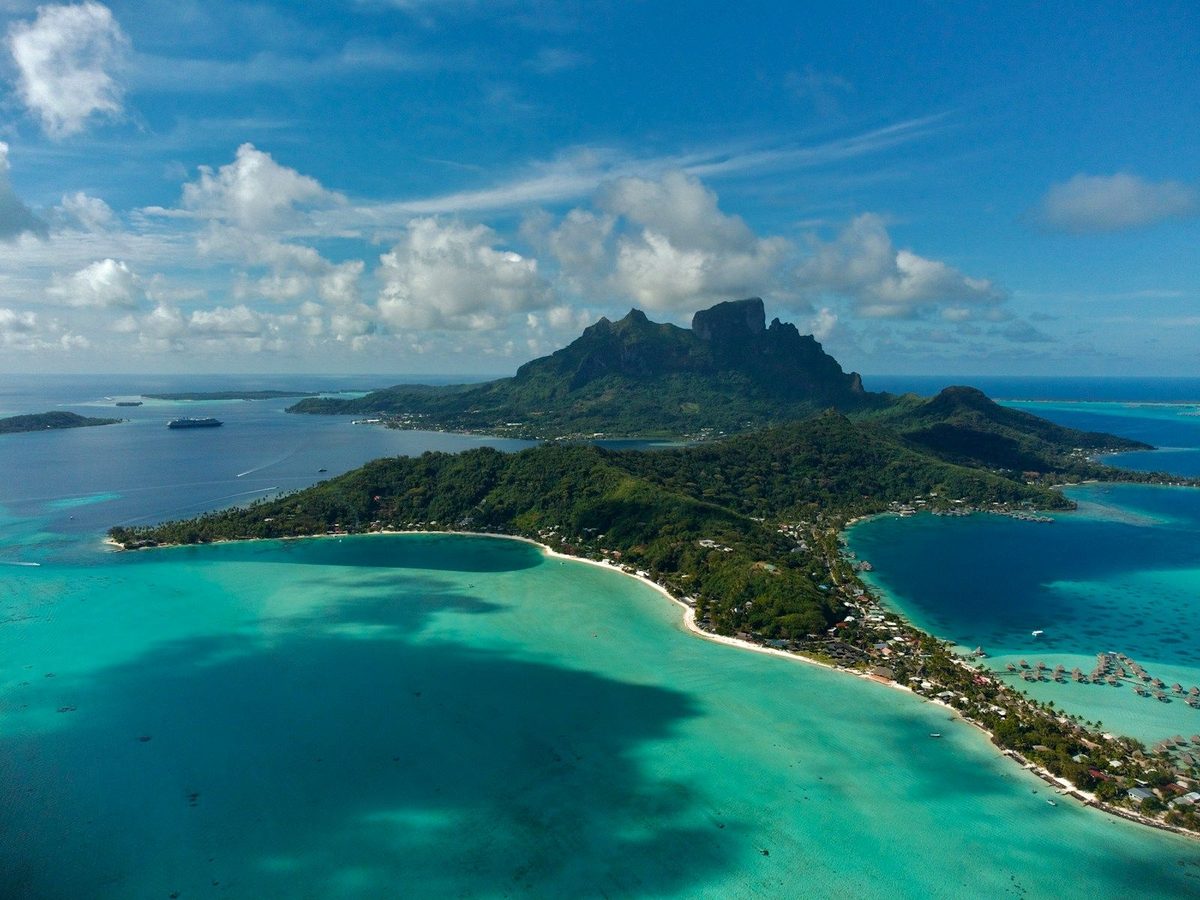 Vista aérea de una laguna turquesa del Pacífico Sur y el arrecife alrededor de una isla volcánica verde en la Polinesia Francesa
