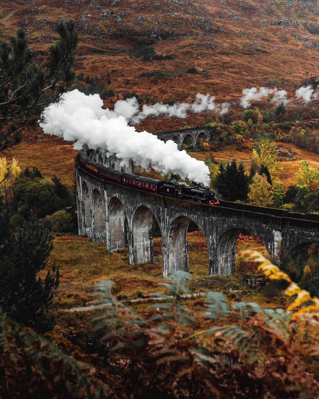 Aerial view of a black steam train crossing the Glenfinnan Viaduct in the Scottish Highlands