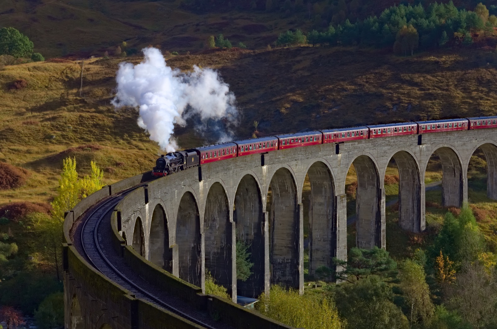 The Jacobite Steam Train crossing Glenfinnan Viaduct with passengers waving from open windows