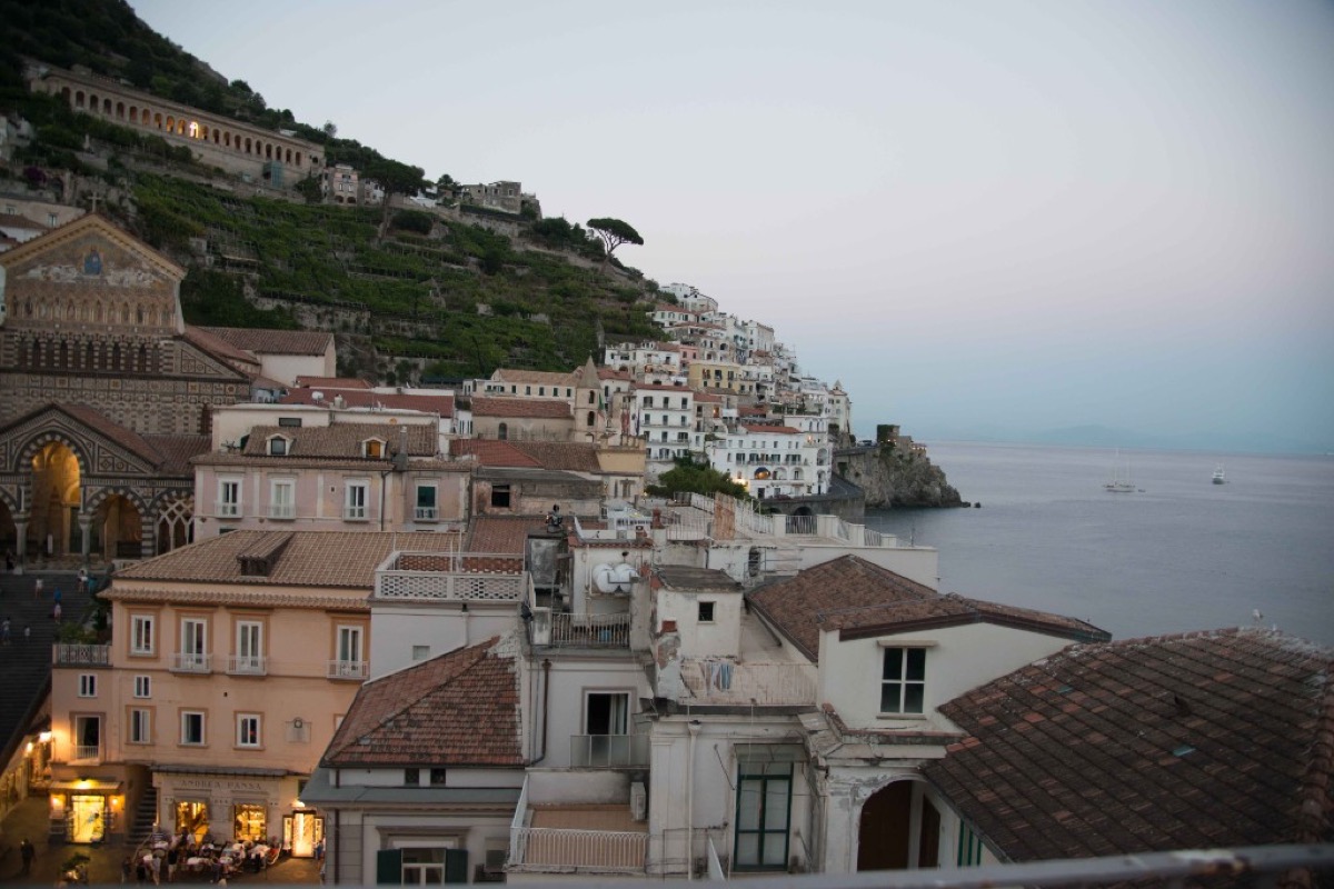 Amalfi at dusk, the striped facade of the Cathedral of Saint Andrew on the left with houses climbing the cliffs to the sea