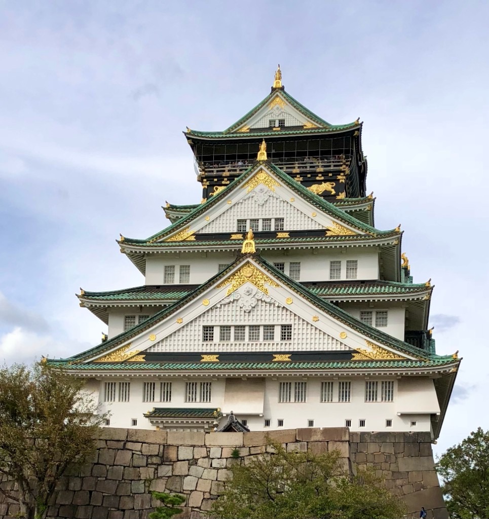Osaka Castle rising above its stone foundation with green tiled roofs and gold accents, Japan