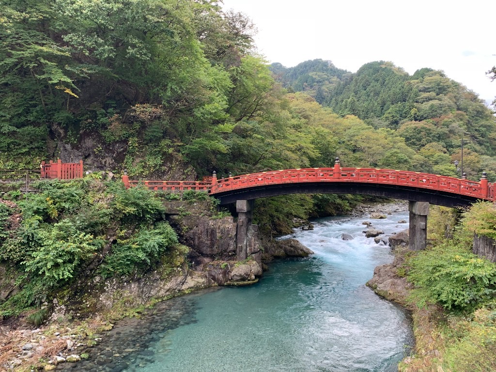 The sacred red Shinkyo Bridge arching over the turquoise Daiya River in Nikko, Japan, surrounded by forested hills