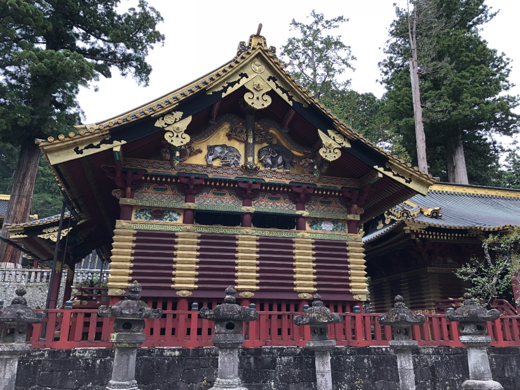 The ornate Kamijinko storehouse at Toshogu Shrine in Nikko, with gold and red walls and carved elephants beneath ancient cedar trees