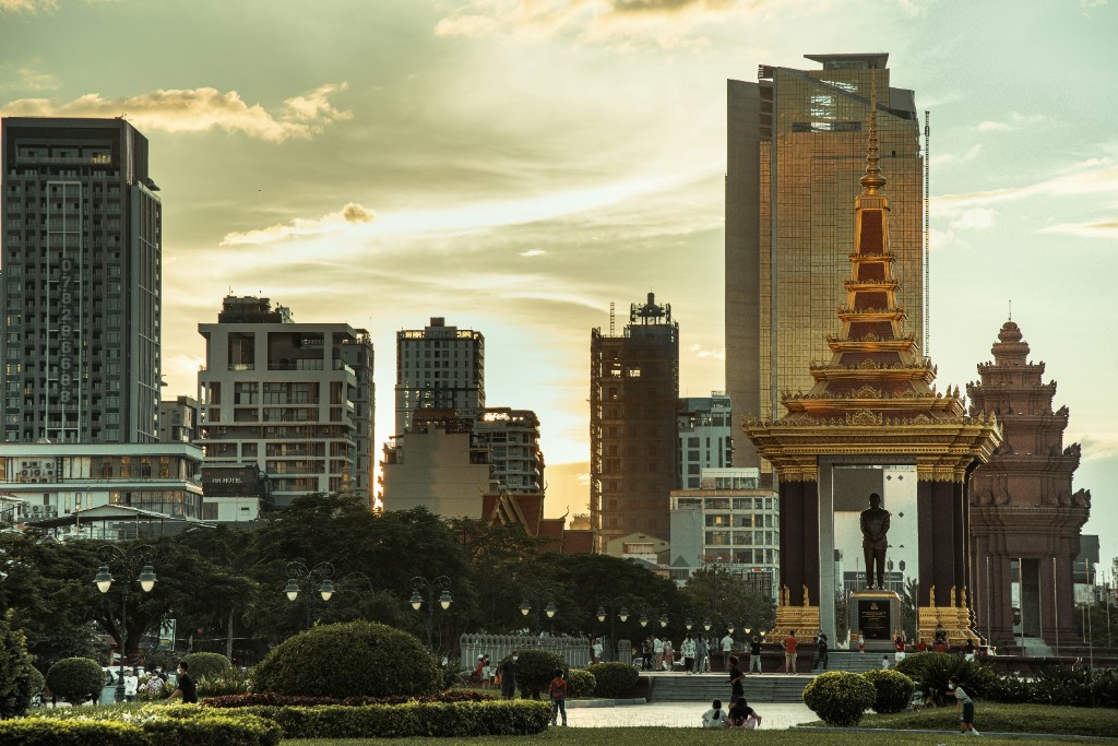 Phnom Penh park and Khmer monuments at sunset with modern skyline beyond