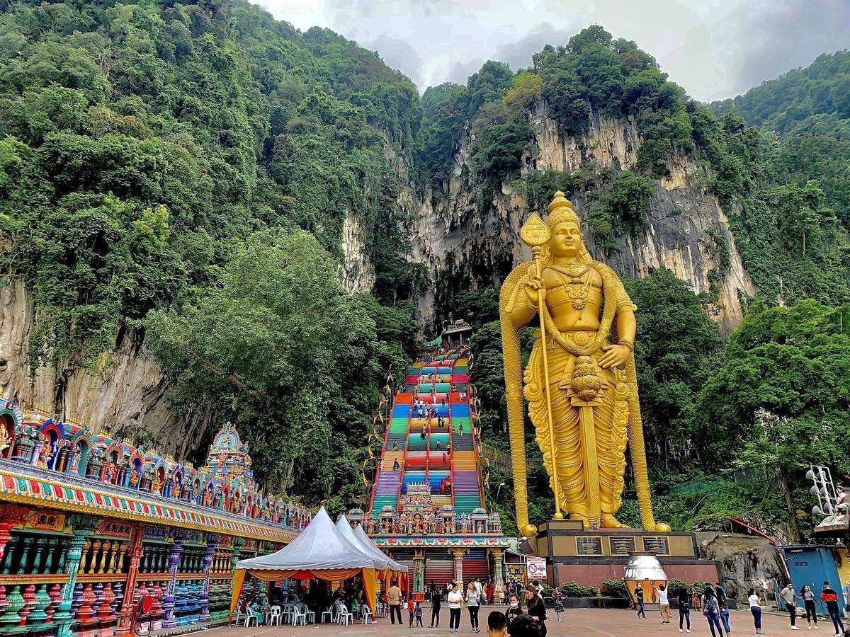 The colourful staircase and golden Lord Murugan statue at Batu Caves, set against limestone cliffs