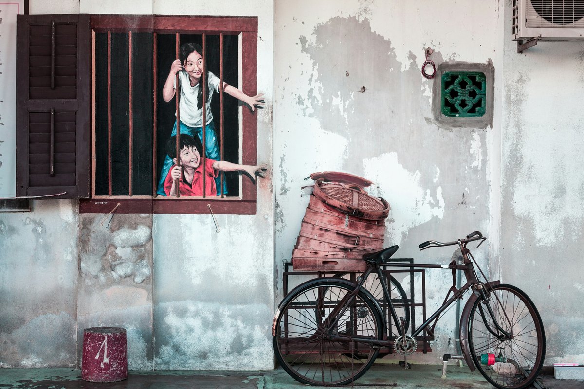 George Town street art of two children at a shophouse window beside a real bicycle, Penang