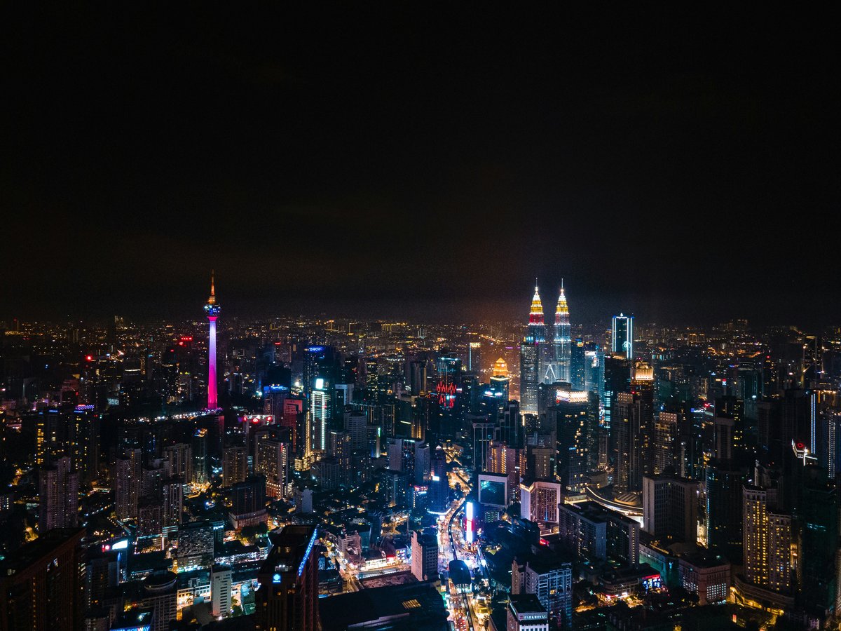 Kuala Lumpur's illuminated skyline at night, with the Petronas Twin Towers and KL Tower