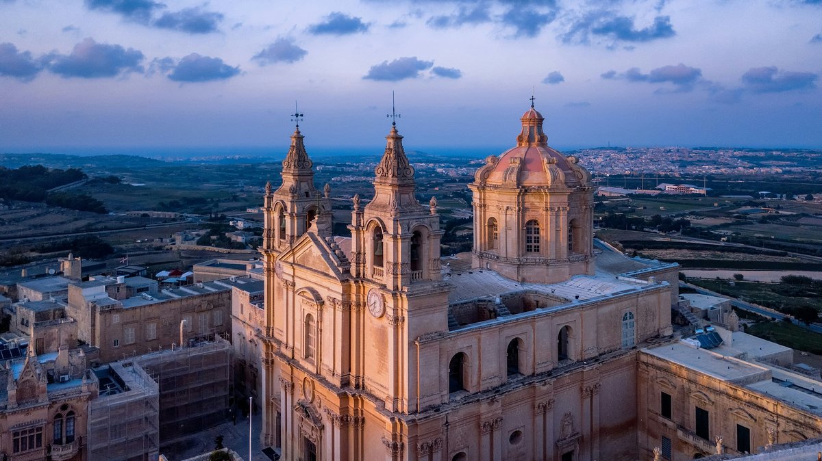Aerial view of Mdina Cathedral at sunset, with the walled city and countryside beyond