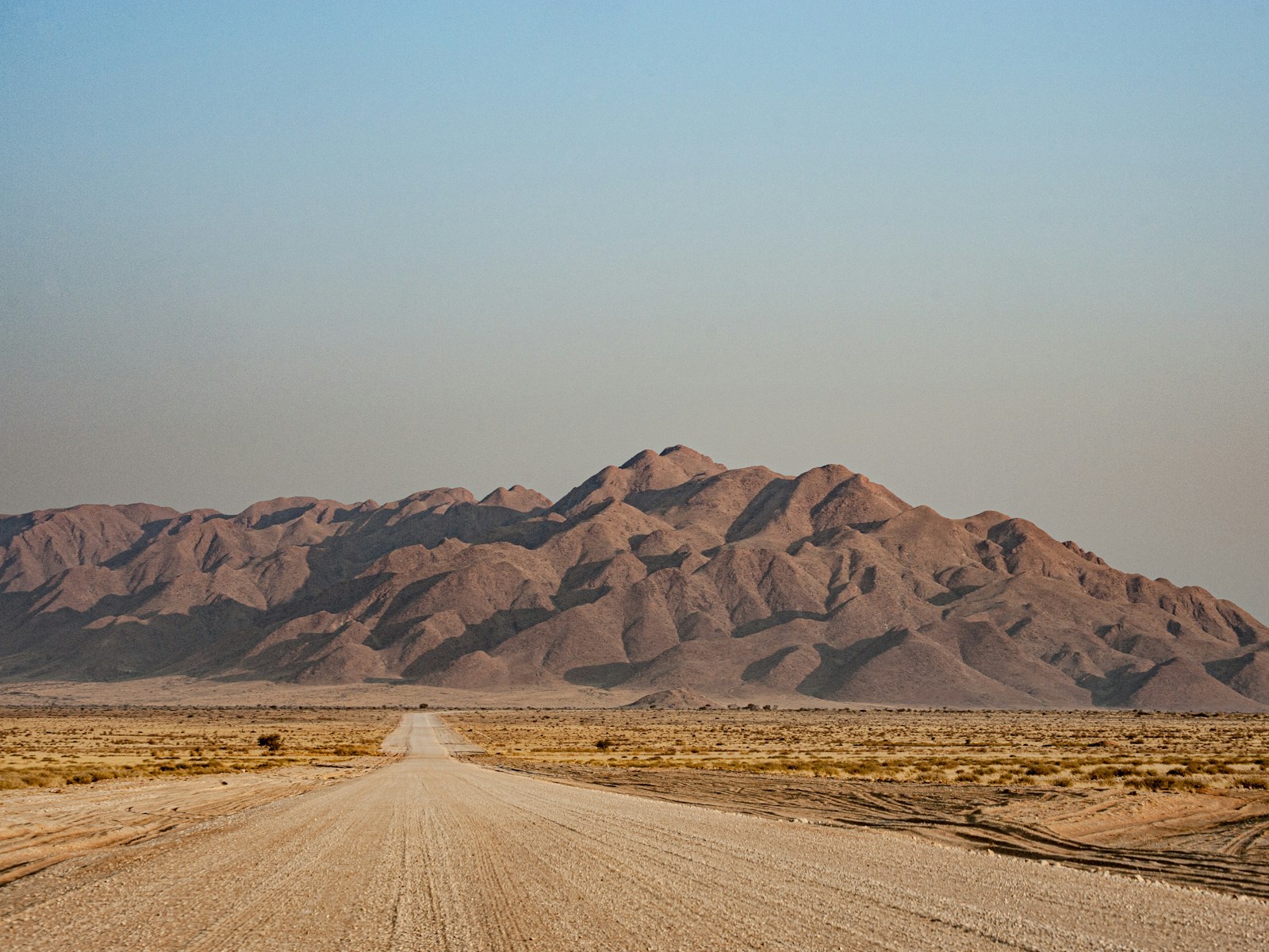 Straight gravel road through arid Namibian plains toward distant mountains