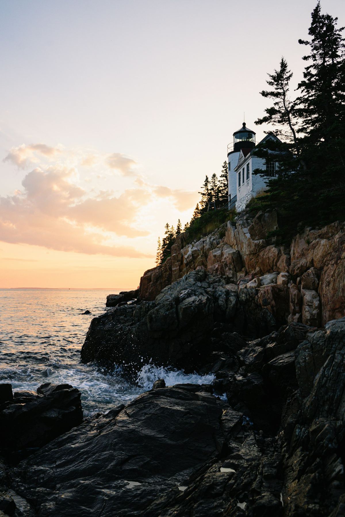 A lighthouse on a rocky shoreline in Acadia National Park, Maine, at sunset