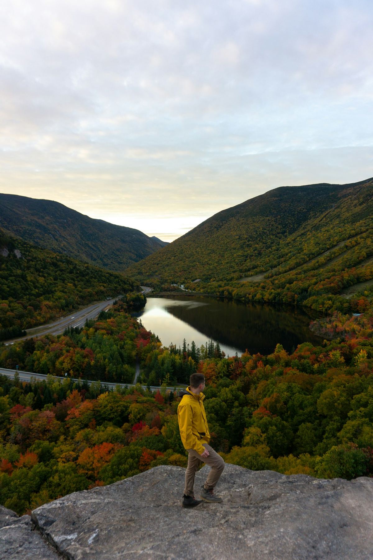 A hiker standing on a rocky outcrop at Artist Bluff in New Hampshire, surrounded by autumn foliage