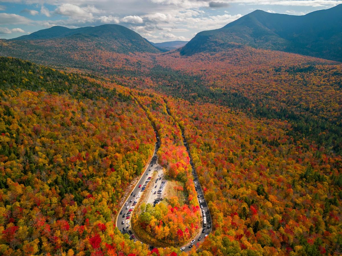 Aerial view of the winding Kancamagus Highway through the White Mountains of New Hampshire during peak fall foliage