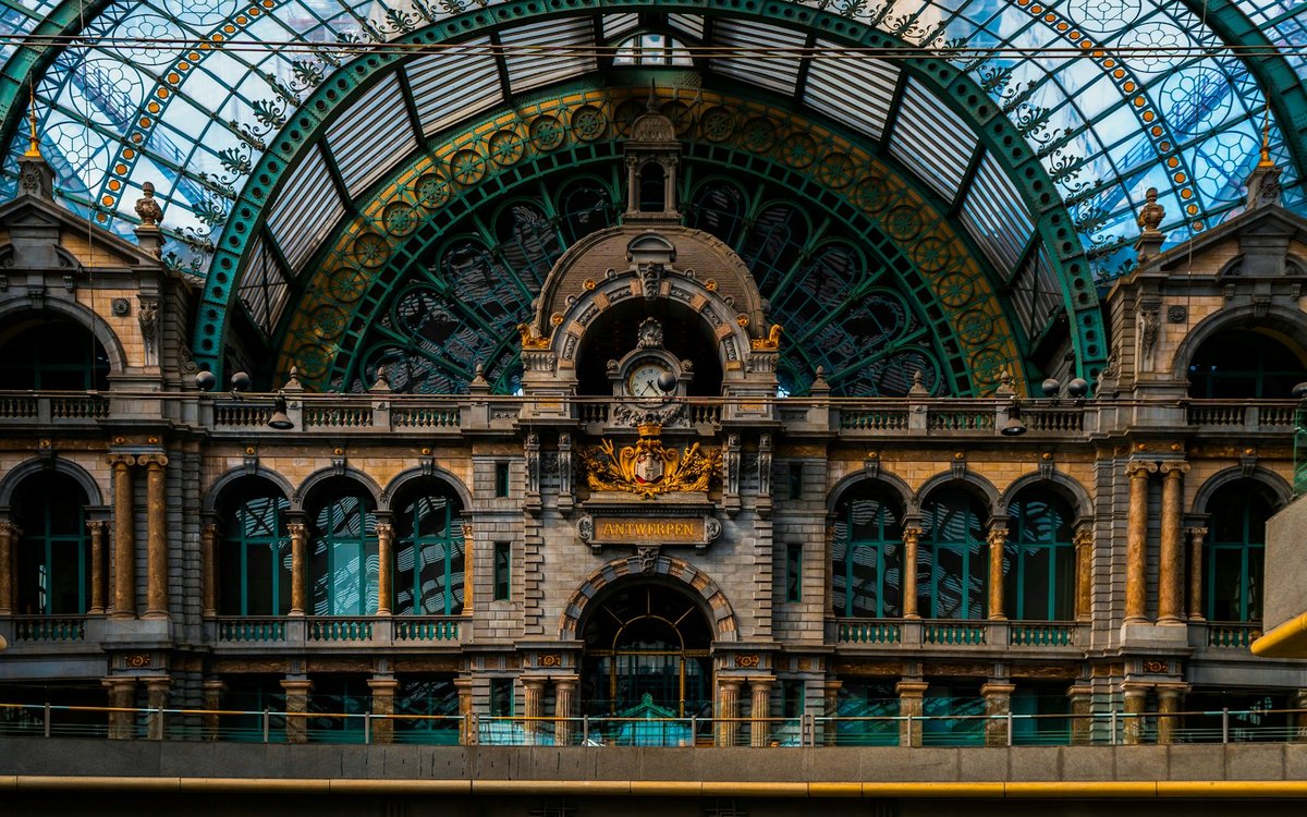時計、石のアーチ、ガラスドームが見えるAntwerpen-Centraal駅の内部