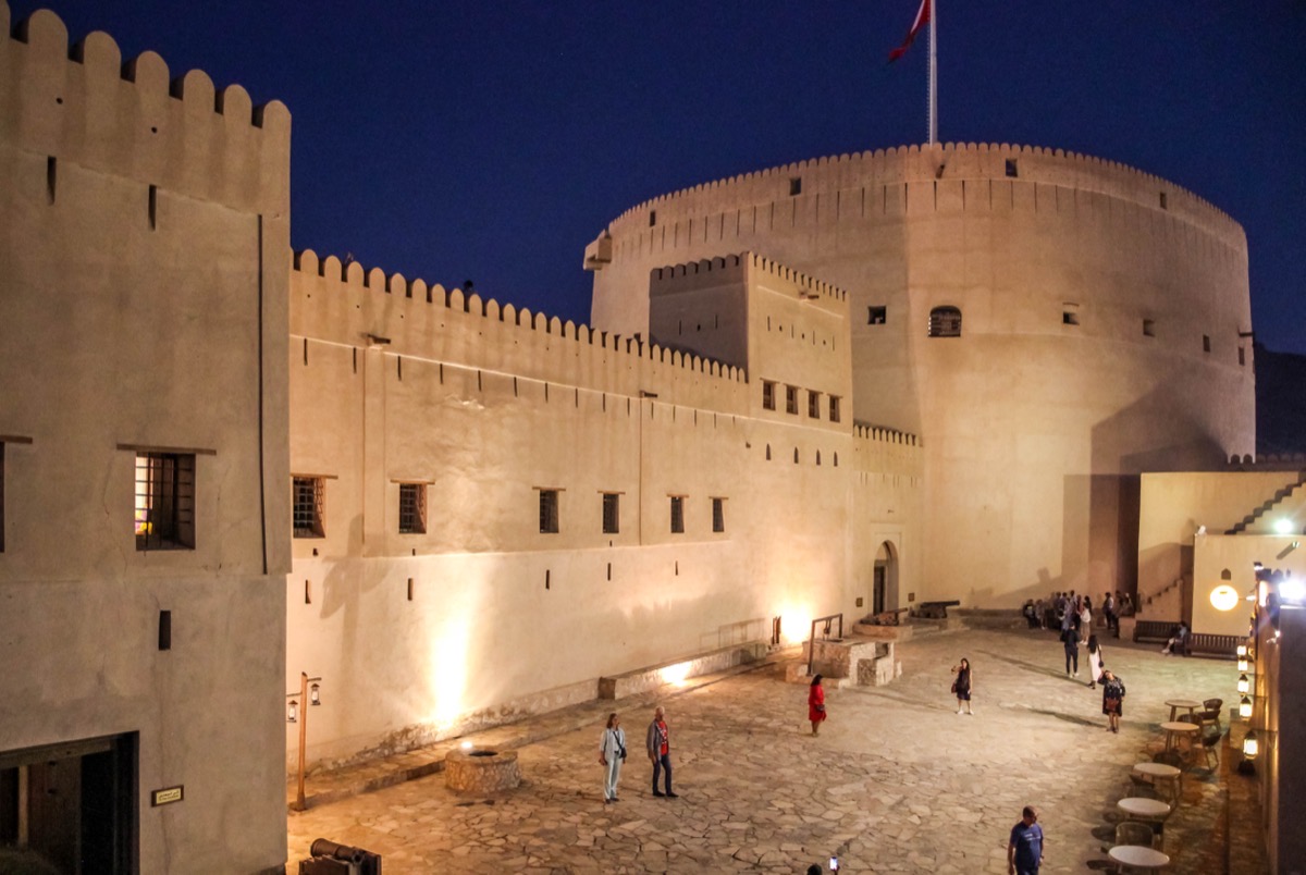 Fort de Nizwa éclairé la nuit avec sa tour circulaire au-dessus des bâtiments environnants