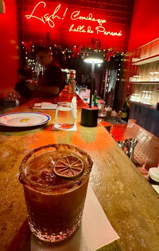 Margarita de tamarindo y mezcal con una rodaja de limón seco en la barra de Fonda Lo Que Hay, bajo un neón rojo que dice Comida que habla de Panamá