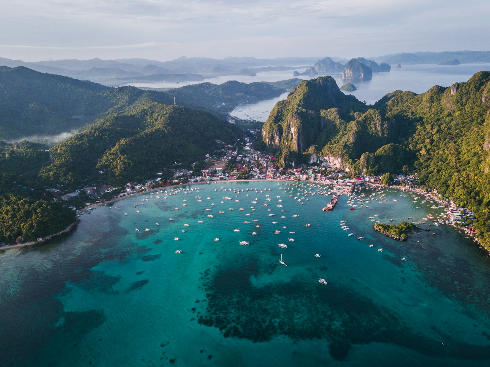 Aerial view of El Nido coastal town and turquoise bay with outrigger boats and limestone mountains