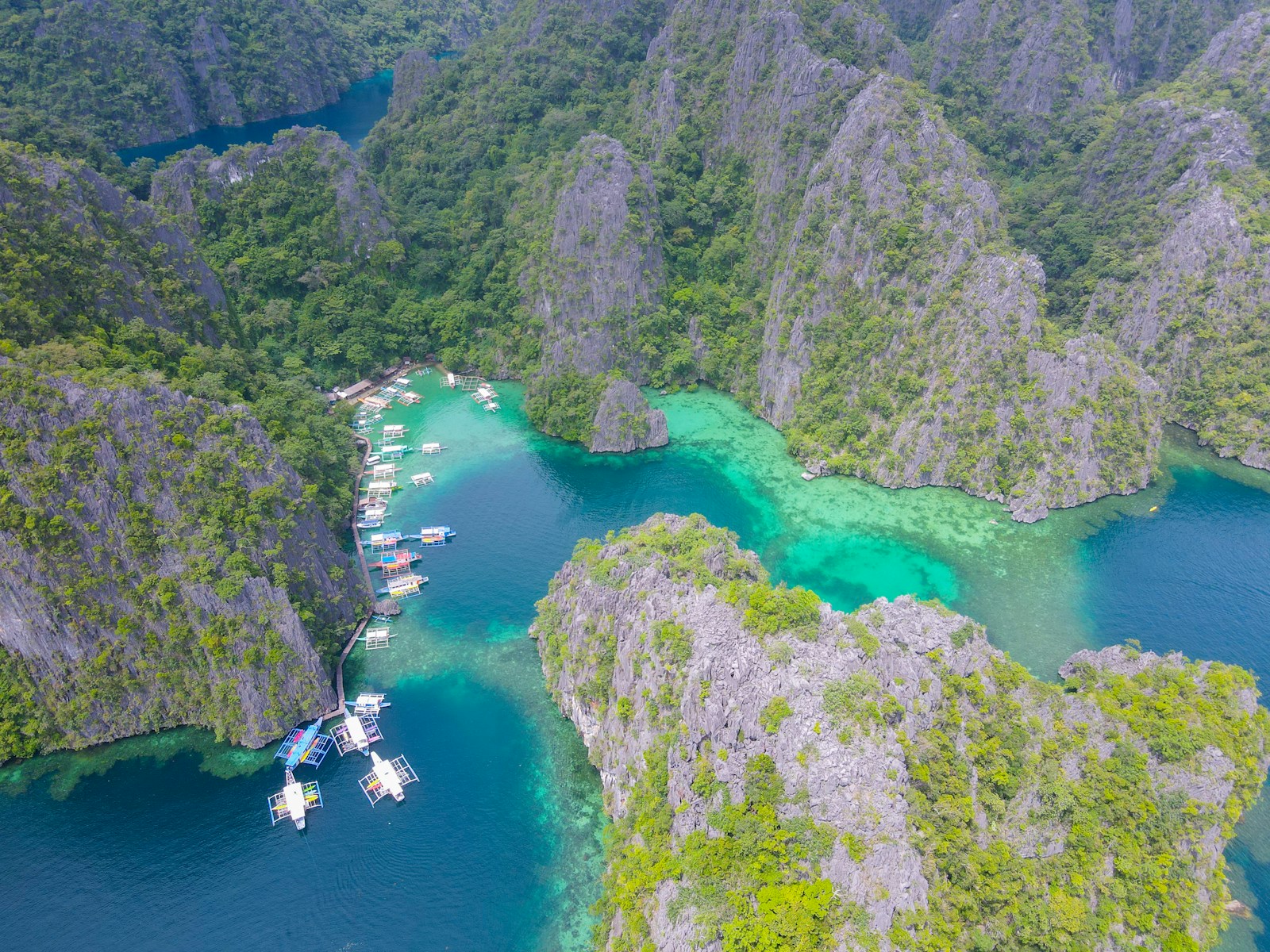 Traditional outrigger boats anchored in a turquoise lagoon surrounded by limestone cliffs in the Philippines