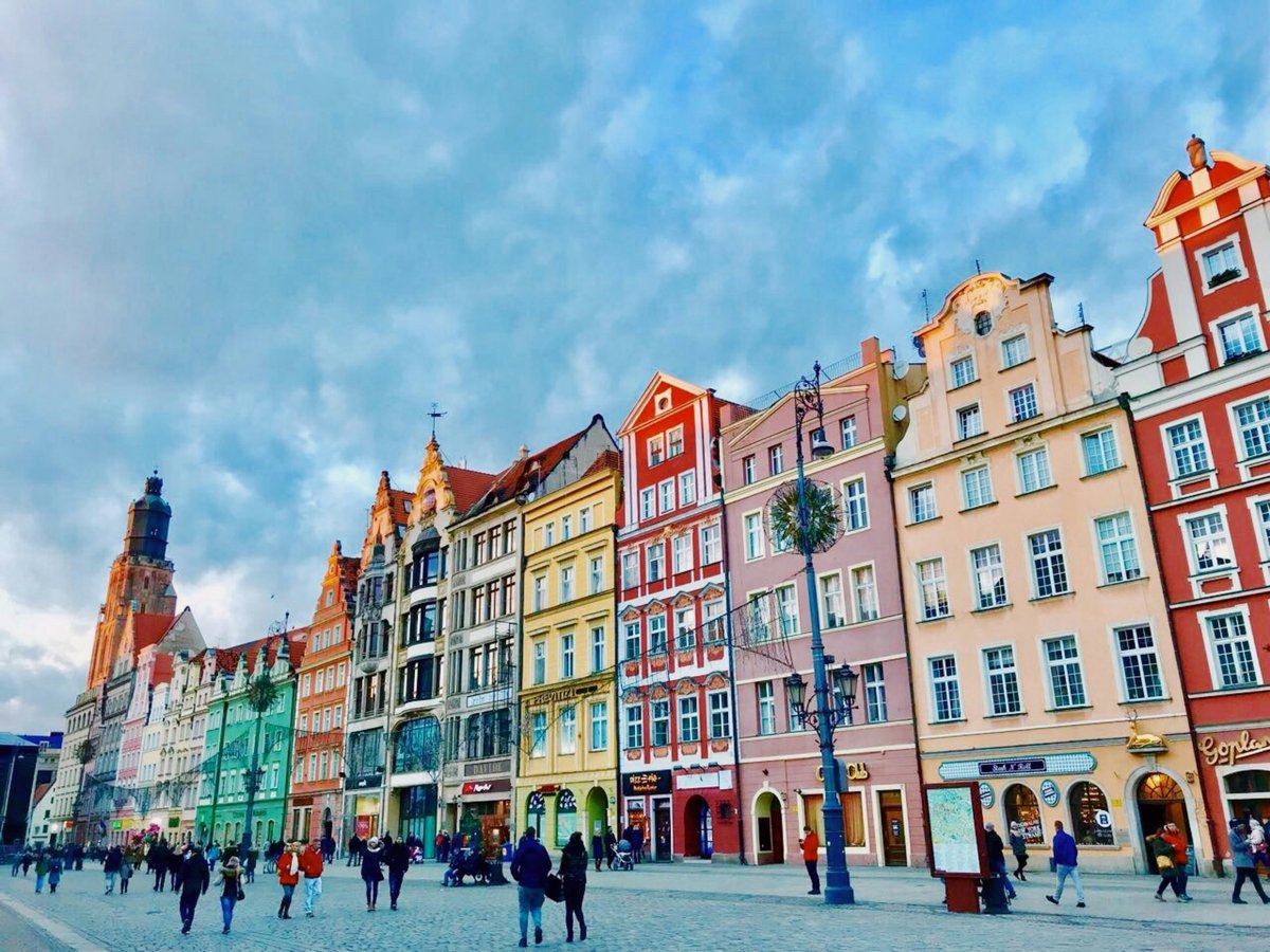 Colourful historic townhouses lining Wrocław's Market Square under a blue sky, with people walking across the square