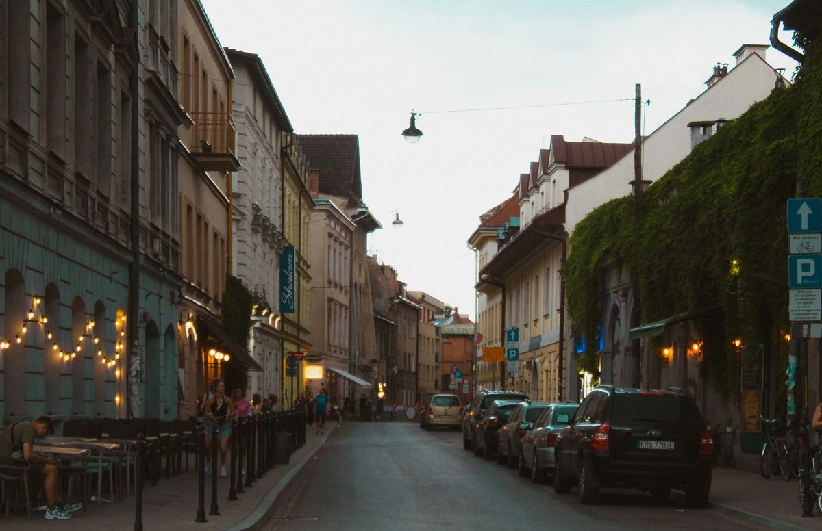 A quiet street in Kazimierz, Kraków, with café lights, ivy-covered buildings and parked cars
