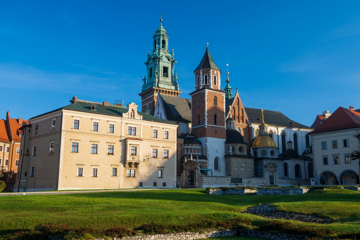 Wawel Royal Castle and Wawel Cathedral with its green and gold domes above a lawn in Kraków