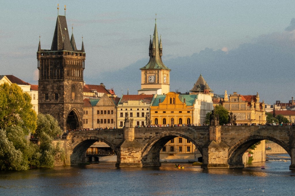 Charles Bridge spanning the Vltava with Old Town Bridge Tower and golden-hour light on Prague’s riverfront