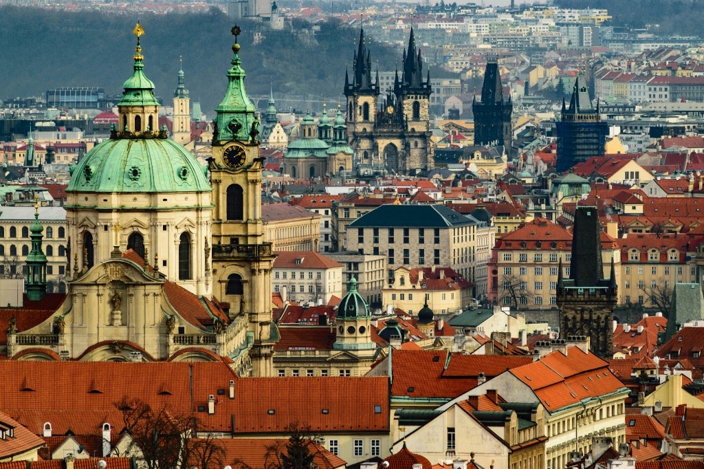 Prague skyline of red rooftops with St. Nicholas Church’s green dome and the twin spires of Týn Church