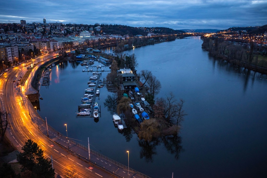 Evening view of the Vltava from above with boats, riverbank lights and Prague hills beyond