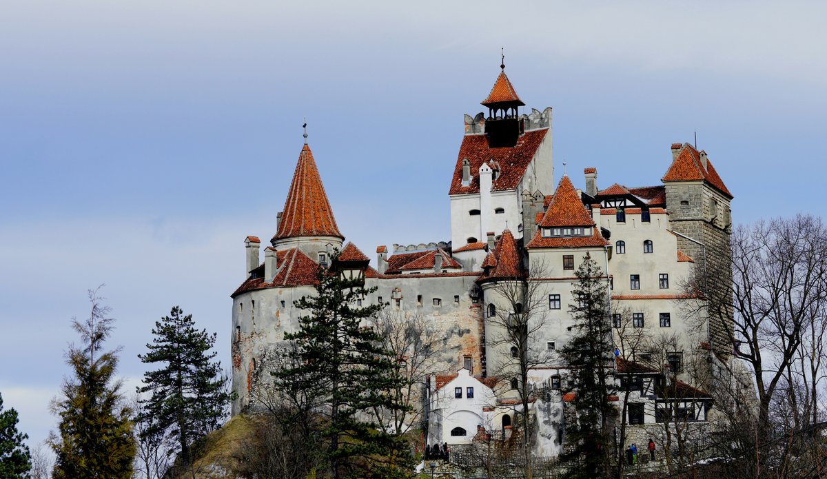 Bran Castle with its white walls and red-tiled turrets on a rocky outcrop, framed by evergreen trees