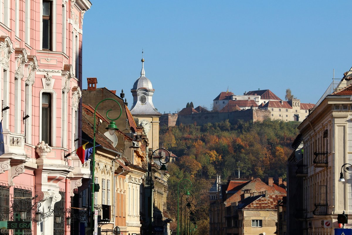 Colourful historic buildings on a street in Brașov's Old Town, with a church tower and autumn-coloured hills behind